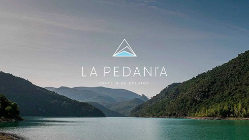 Paisaje de un lago rodeado de montañas verdes, con cielo despejado, promocionando La Pedanía, espacio de eventos en España, ideal para celebraciones y actividades al aire libre.